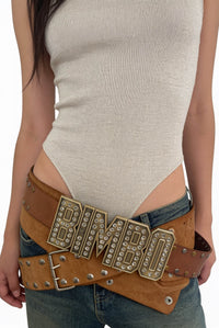Model wearing the Bimbo Belt in tan, a wide leather belt with a rhinestone BIMBO buckle, over low-rise jeans