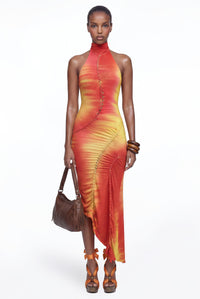 Model wearing the Senja Dress in Inferno, a sunset ombré halter maxi dress with macramé detailing and an asymmetric hem